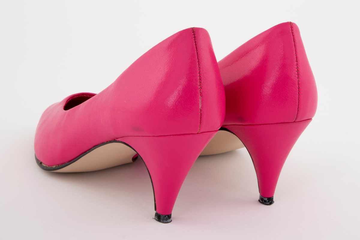 Sjokkrosa pumps med moderat høy stiletthæl. Syntetskinn, fôret med tekstil, alt sterkt rosa. Lys beige syntetsåle og svart plastflikk. Både ringning og tå er ganske spisse. Ingen synlig søm på utsiden av ringningen. Polstret binnsåle, dvs en mellomsåle av skumgummi. Str. 39