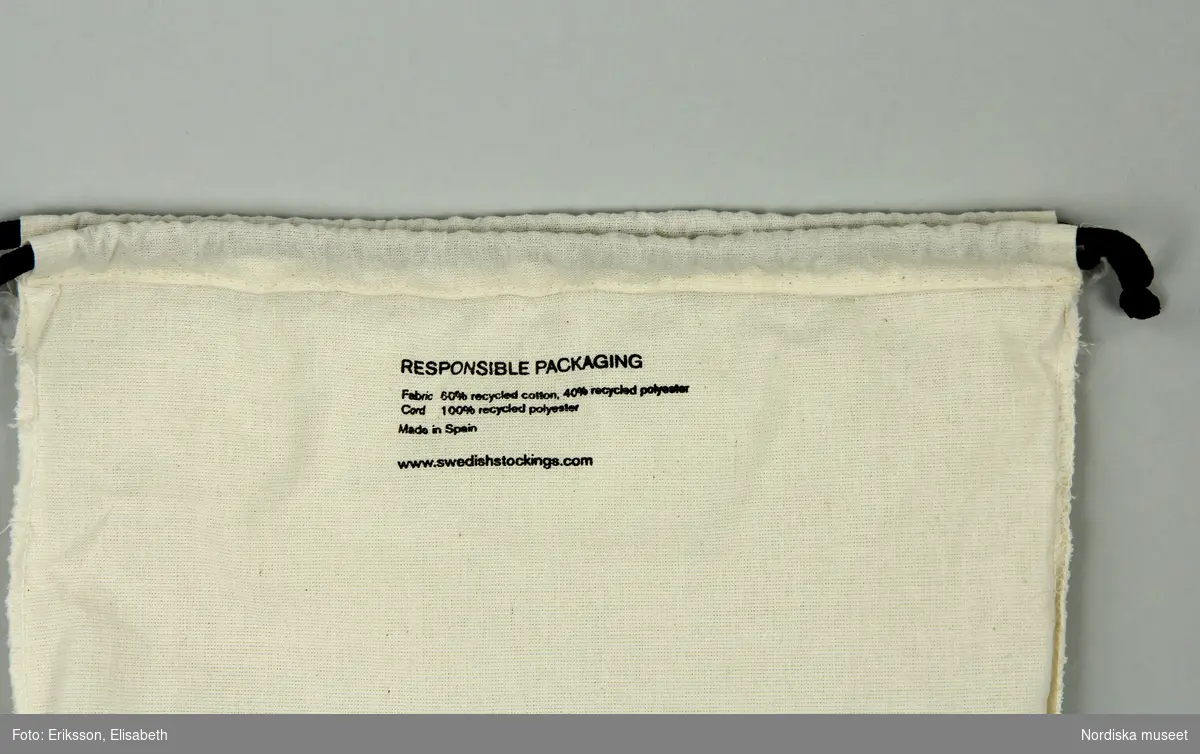 Påse av textil, vit (off white), rektangulär med dragsko av svart snöre i ena kortsidan. Text på ena sidan "SWEDISH STOCKINGS", samt på insidan av påsen: "RESPONSIBLE PACKAGING / Fabric: 60% recycled cotton, 40% recycled polyester. Cord: 100% recycled polyeseter / Made in Spain / www.swedishstockings.com"
/Leif Wallin 2024-06-26