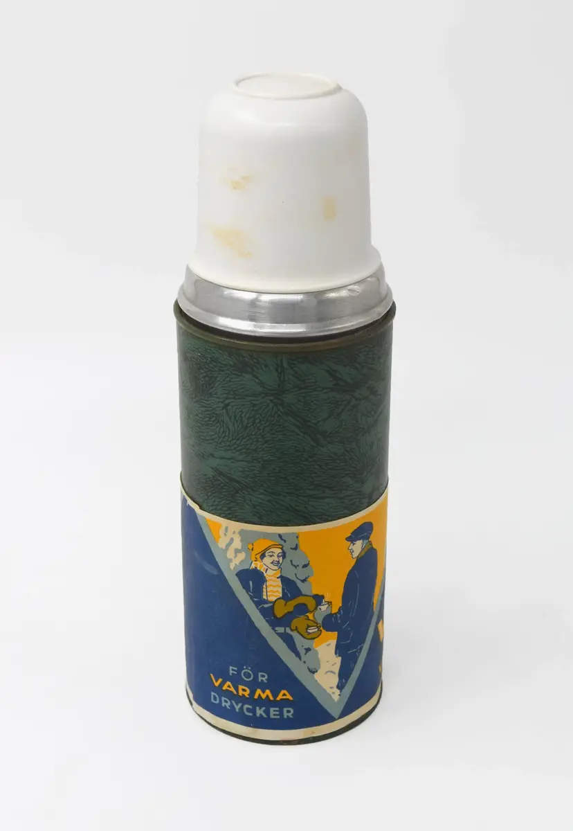 Termos inklädd i grönt marmorerat papper och vitt plastlock. Nedre delen illustrativ bred border som löper längs flaskans omkrets i färgerna gult, blått (ljus och mörk) samt vitt. 

Mitten visar ett isblock med en eld under och texten: "VA-KA FLASKAN VARMT och KALLT". 
Till vänster om denna illustration, en man och kvinna i vinterkläder med vinterlandskap bakom. Kvinnan häller över dryck från en termos till mannens dryckeskärl. Tillhörande text: " FÖR VARMA DRYCKER".
På andra sidan, en man i byxor och tröja samt en kvinna med klänning på en båt. Kvinnan häller över dryck från en termos till mannens dryckeskärl. Tillhörande text: " FÖR KALLA DRYCKER".

Öppningen av termosen stängs med en kord och därefter det vita plastlocket. 

