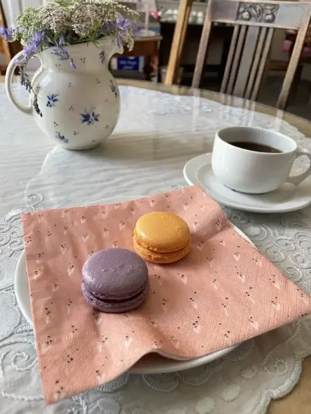 Nærbilde av to makroner på en en tallerken med rosa serviett. Den ene makronen er lilla og den andre er oransje.