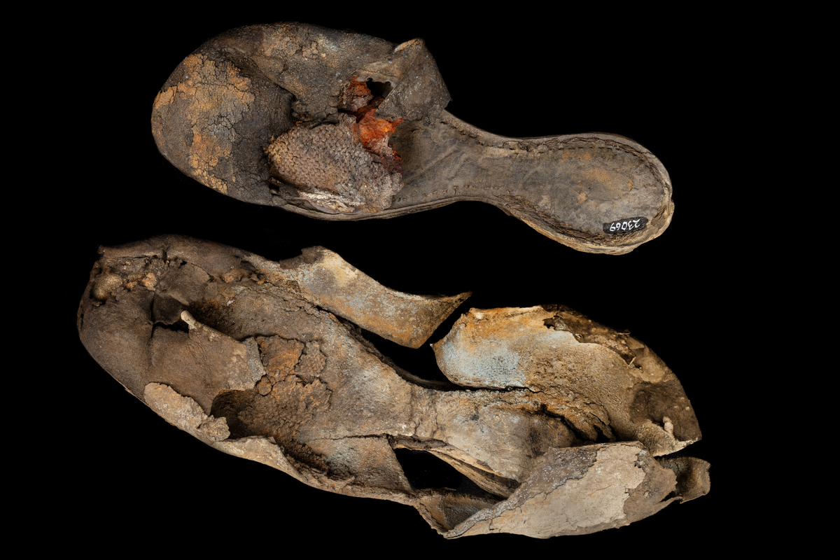 Dokumentation 1996:
Delar och fragment av sko: en skobotten samt ett fragmentariskt ovanläder, tre bitar av ett filtliknande material, ett 15-tal fragment av bottenläder samt sex mindre fragment av trä.
Skobottnen har kvarsittande tråd och träpligg. Yttersulan är ritsad. Klacken består av fem klacklappar som är placerade mellan ytter- och innersulan. Innersulans läder är mycket kraftigt, ca 6 mm tjock. Ovanlädret är sprött och fragmentariskt samt har blå och rostfärgade utfällningar.

Text in English: 
Various parts and fragments of a shoe, consisting of a sole with fragments of vamp (upper leather), three pieces of a felt-like material, some 15 fragments of sole or bottom leather and six smaller fragments of wood.
There are remains of thread and wooden pegs on the shoe sole. The outsole is channeled. The heel is made up of five heel lifts placed between the insole and outsole. The leather of the insole is very thick, ca 6 mm. The upper leather is fragile and fragmentary, and has blue and rust-coloured precipitations.

Dokumentation 2022:
Skobotten och delar av ovanläder till en öppen randsko. Tillverkade i getskinn av god kvalitet. Skapades på en rak läst och bars på höger fot. Klacken som är lagad med en läderlapp under sulan. Inga dekorationer. Det finns tecken på delaminering. Fragment från en stickad strumpa hittades inuti skon. Det finns lagningar med träpligg på sulan och hälen. Skobotten hör ihop med fyndnummer 23070.
För mer information, se Länkade filer: Uppritning

Text in english:
This is the bottom unit and upper fragments of an open shoe, made of goatskin leather of good quality, of randed construction with a patch heel, made on a straight last and worn on the right foot, with no decorative features. The bottom unit pairs with 23070. There are signs of delamination and fragments of a knitted stocking were found inside the shoe. There are pegged repairs to sole and heel.
For more information, go to Länkade filer: Uppritning