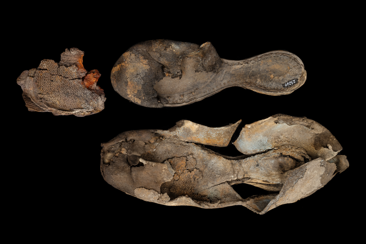 Sko.
Inuti skorna hittades även fragment från olika textilier som ursprungligen varit ett par strumpor. Idag sitter ett stickat fragment av ull fast i vänsterskon (23070) med avigsidan uppåt. I fyndet finns även en mängd lösa stickade fragment som idag är mycket korroderade och vissa helt mineraliserade av järn vilket har gjort textilen stenhård och därmed oerhört skör (23070a-c). Utifrån minskningar som några små fragment har så har det varit möjligt att rekonstruera strumpans tå. Genom att pussla ihop fragmenten som ursprungligen har suttit ihop har det på så vis gått att avgöra hur strumpans tå har varit konstruerad. Då textilen är så fragmentarisk är det inte möjligt att avgöra hur resten av strumpan har sett ut eller varit konstruerad. Däremot så finns det fragment av ett kypertvävt tyg av ull som på vissa ställen ligger dubbelt med det stickade 23070c). Ett av dessa fragment har stelnat i formen så som den suttit på fotens främre del inuti skon. Detta fragment täcker delvis det stickade tyget och har dessutom spår av kaststygn längs en kant. Så som det vävda tyget är placerat på det stickade tyget pekar på att man använt det som lagningslappar till sina stickade strumpor. 
I fyndet finns det även korroderade järnklumpar, ett tuskaftsvävt tyg av ull och rester av ett grovt bastfibergarn och två mindre läderfragment (23070d-f). Det är möjligt att även dessa har tillhört strumpan och/eller skon.

För mer detaljerad information från textildokumentationen (år 2022) se länkade filer.

Skodokumentation 2022:
Ovanläder. Tillverkad i getskinn av god kvalitet. Hör ihop med fyndnummer 23069 (Yngves skor). Tillverkades på en rak läst och bars på vänster fot. Inga dekorationer Det finns stygnhål som visar att det funnits invändiga förstärkningar (men förstärkningslappen saknas). Det finns delaminering men inga lagningar.
För mer information, se Länkade filer: Uppritning

Text in english:
This is the upper of a shoe of more “extreme fashion”, made of goatskin leather of good quality, probably made on a straight last and worn of the left foot, with no decorative features. The upper couples with 23069, together composing Yngve’s shoes. There are internal reinforcements missing from the upper and delamination, there are no repairs.
For more information, go to Länkade filer: Uppritning