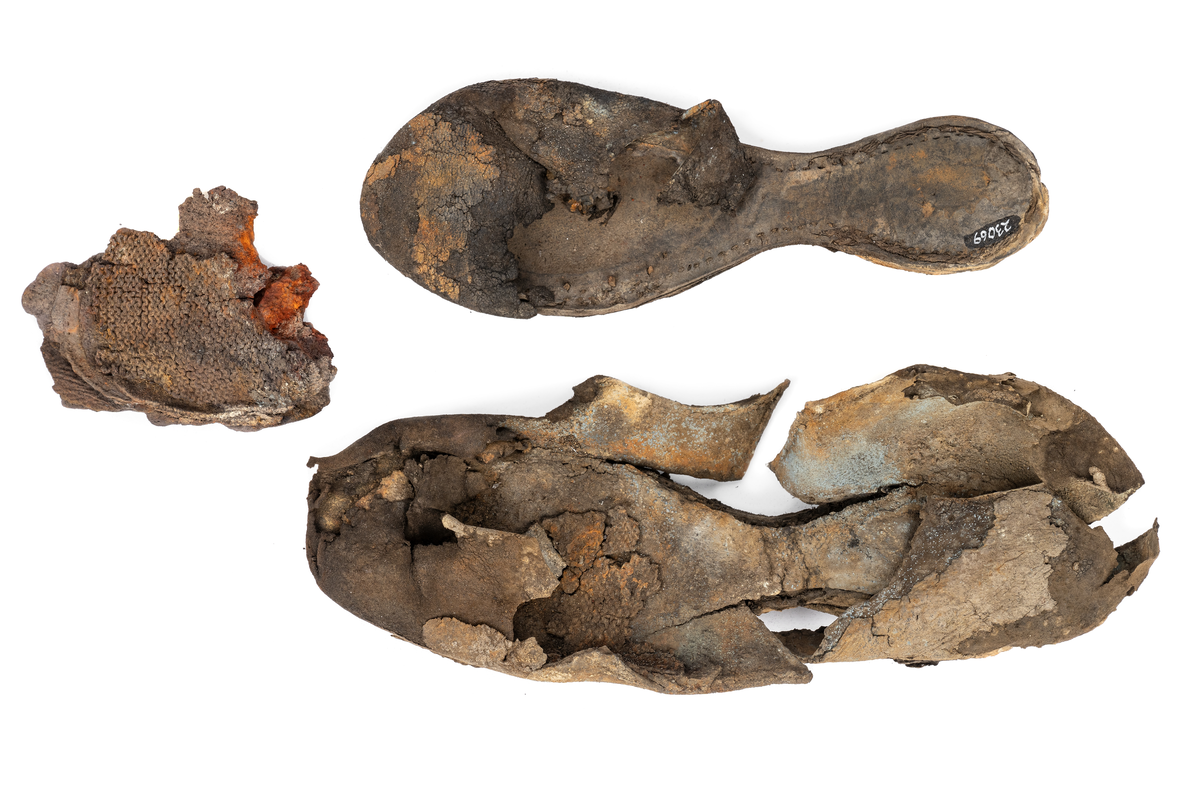Dokumentation 1996:
Delar och fragment av sko: en skobotten samt ett fragmentariskt ovanläder, tre bitar av ett filtliknande material, ett 15-tal fragment av bottenläder samt sex mindre fragment av trä.
Skobottnen har kvarsittande tråd och träpligg. Yttersulan är ritsad. Klacken består av fem klacklappar som är placerade mellan ytter- och innersulan. Innersulans läder är mycket kraftigt, ca 6 mm tjock. Ovanlädret är sprött och fragmentariskt samt har blå och rostfärgade utfällningar.

Text in English: 
Various parts and fragments of a shoe, consisting of a sole with fragments of vamp (upper leather), three pieces of a felt-like material, some 15 fragments of sole or bottom leather and six smaller fragments of wood.
There are remains of thread and wooden pegs on the shoe sole. The outsole is channeled. The heel is made up of five heel lifts placed between the insole and outsole. The leather of the insole is very thick, ca 6 mm. The upper leather is fragile and fragmentary, and has blue and rust-coloured precipitations.

Dokumentation 2022:
Skobotten och delar av ovanläder till en öppen randsko. Tillverkade i getskinn av god kvalitet. Skapades på en rak läst och bars på höger fot. Klacken som är lagad med en läderlapp under sulan. Inga dekorationer. Det finns tecken på delaminering. Fragment från en stickad strumpa hittades inuti skon. Det finns lagningar med träpligg på sulan och hälen. Skobotten hör ihop med fyndnummer 23070.
För mer information, se Länkade filer: Uppritning

Text in english:
This is the bottom unit and upper fragments of an open shoe, made of goatskin leather of good quality, of randed construction with a patch heel, made on a straight last and worn on the right foot, with no decorative features. The bottom unit pairs with 23070. There are signs of delamination and fragments of a knitted stocking were found inside the shoe. There are pegged repairs to sole and heel.
For more information, go to Länkade filer: Uppritning