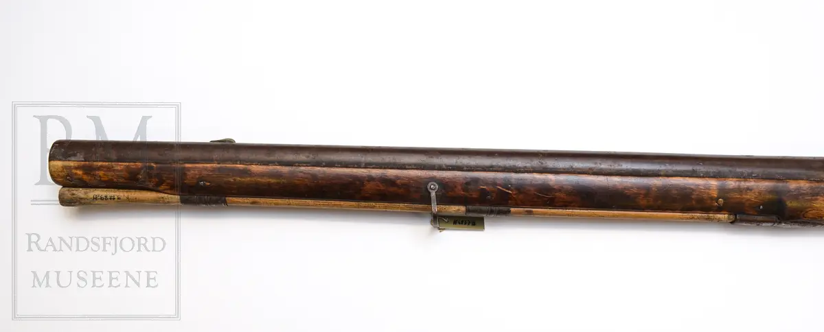 Munnladning, glattløpet m/ perkusjonslås. Skjefte av tre, brunbeiset. Kolben har kinntre og utskjæringer (nettskjæring) på kolbehalsen. Pipe og lås av jern m/ fram og baksikte i messing. To rembøyler med skruer. Ladestokk (b)  av tre er festet under forskjeftet. Bøylebeslag, avtrekkerbøyle mangler. gjennomgående skrue mellom beslag bak pipe og avtrekkerbeslag mangler. Forskjeftet går helt fram til pipemunningen. Har ikke bajonett. Pipen er rund framme og åttekantet bak. Grovkalibret.