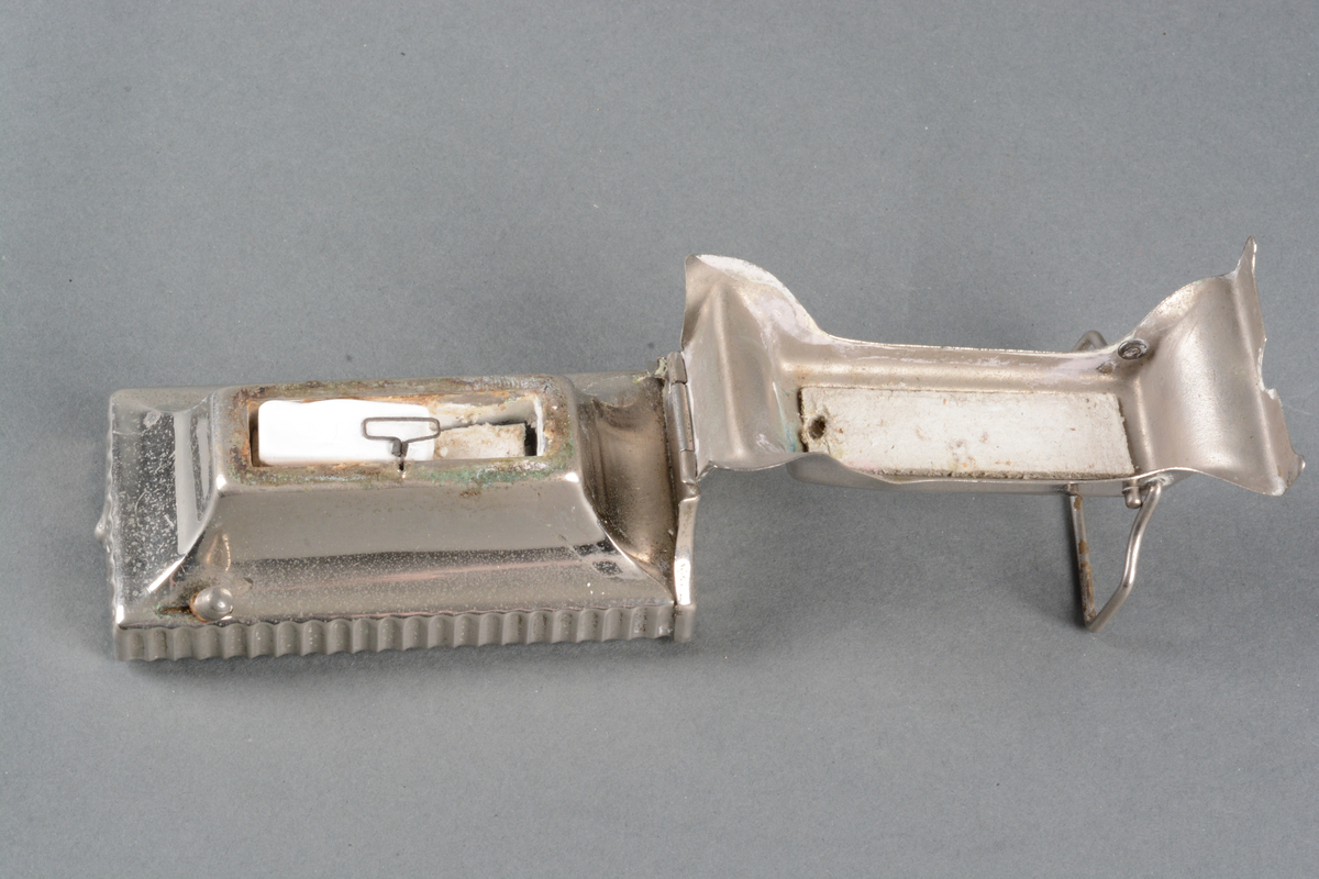 Krølltangvarmer med metatablett, laget av forniklet metallplate med hengslet lokk som fungerer som holder for en krølltang. Det ligger en metatablett i.