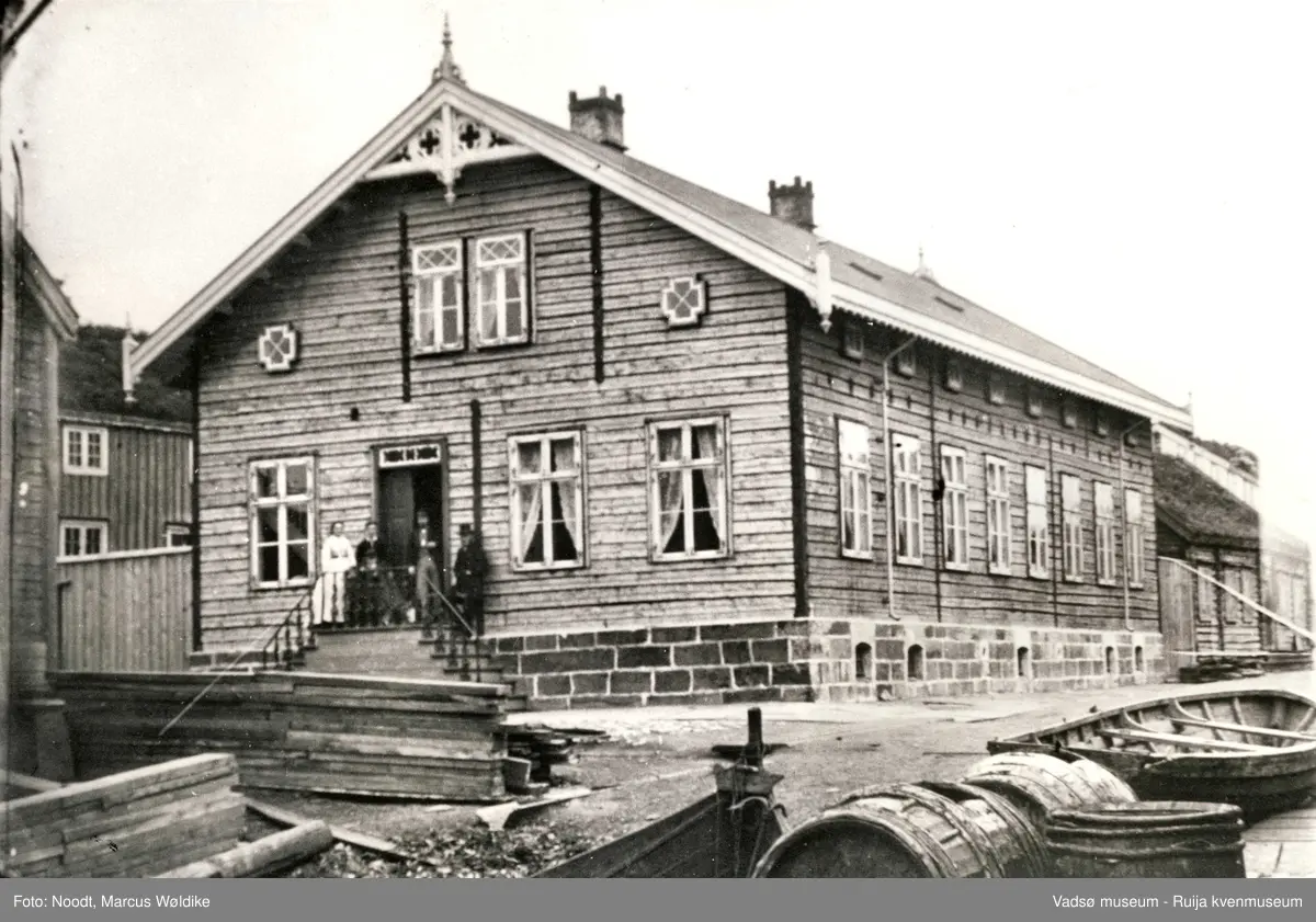 Brodtkorbgården i Hvistendahlsgt. i Vadsø ved byens gamle torg.  Fasaden mot Tollbogt. med folk på trappa, 1864.