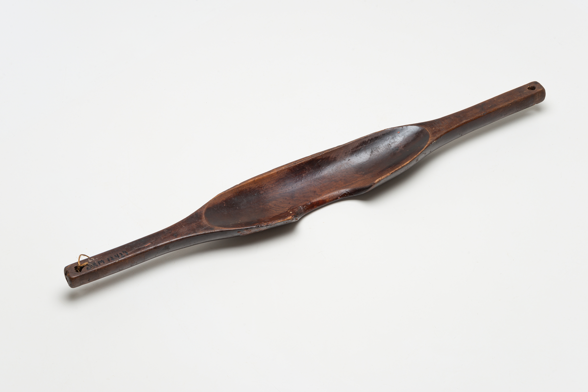 Vannåk av tre. Avlangt trestykke med avsmalnende ender, på midten en utskåret fordypning til skulder og nakke. Hull i bære stropper i begge ende.