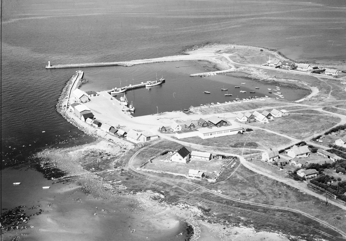 Flygbild. Glommens hamn med fiskebåtar och fritidsbåtar, magasin, sjöbodar och omgivande bostadsbebyggelse. Ute på näset står Glumstenen, flyttblocket från istiden som gett fiskeläget Glommen sitt namn, anlagt på 1880-talet. Till en början kallades då både stenen och platsen för Glummen. Stenen har varit ett landmärke för sjöfarare i alla tider. I isländska skrifter benämns den som Glaumstein. Ordet "glum" stammar från något av de fornnordiska orden glaumr, glumr som betyder larma, bullra. Förr användes ordet "bullersten" om flyttblock (på engelska "boulder"), vilket också har koppling till ordet "bumling".