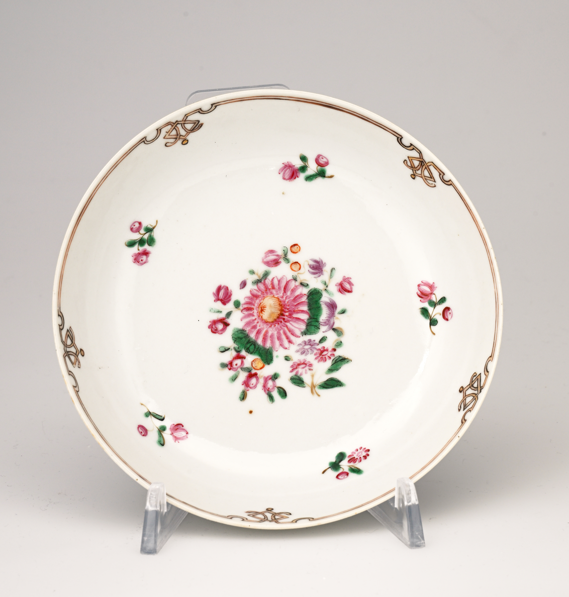 Et tefat av porselen. Det er relativt dypt. På midten er det et sammensatt blomstermotiv i rosa, grønt, lilla og gult. Rundt dette motivet er det fem enkle blomster med stilk/blader. Langs kanten er det en gulbrun bord med markert med svart. Det er fem "utsmykninger" i borden. 
Fatet er del av et teservise av porselen. Det består av 11 kopper og 10 skåler/tefat. Det er av fint porselen som er produsert i Kina i perioden 1750 - 1800 (se FTT.06361, FTT.06361.01-22 for samlet servise og enkeltdeler).
