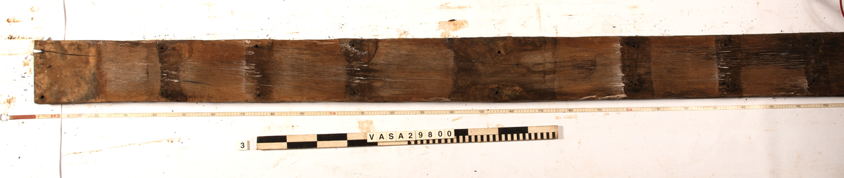 Däcksplanka.
27 genomgående spikhål. Spikhålen är original från när skeppet byggdes. Originalspikarna är bortrostade. Efter bärgningen monterades däcksplankan med rostfri fransk träskruv samt bricka. Vid demonteringen 2023 lossades alla skruvar. De brickor som gick att ta bort togs bort. En del satt så djupt i träet att det inte gick att demontera dem utan att skada plankan. Dessa brickor fick därför sitta kvar. 
Tydliga avtryck från balkar och ribbor på undersidan som även är täckt av ytliga sprickor och har rostfläckar.