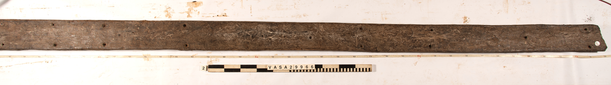 Däcksplanka.
Ena änden är snedskuren.
34 genomgående spikhål. Spikhålen är original från när skeppet byggdes. Originalspikarna är bortrostade. Efter bärgningen monterades däcksplankan med rostfri fransk träskruv samt bricka. Vid demonteringen 2023 lossades alla skruvar. De brickor som gick att ta bort togs bort. En del satt så djupt i träet att det inte gick att demontera dem utan att skada plankan. Dessa brickor fick därför sitta kvar. 
En trädymling i ena änden.
Tydliga avtryck från balkar och ribbor på undersidan som även är täckt av ytliga sprickor och har fläckar av rost.