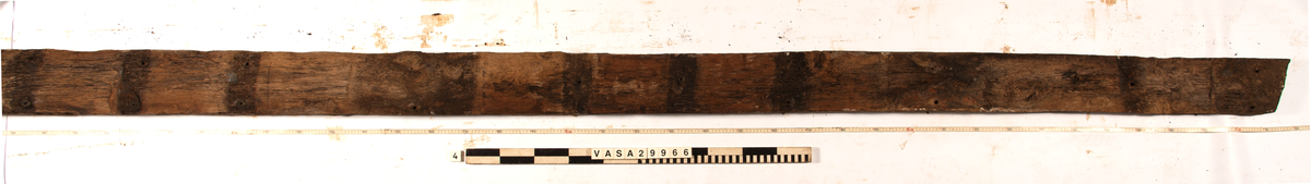 Däcksplanka.
Ena änden är snedskuren.
34 genomgående spikhål. Spikhålen är original från när skeppet byggdes. Originalspikarna är bortrostade. Efter bärgningen monterades däcksplankan med rostfri fransk träskruv samt bricka. Vid demonteringen 2023 lossades alla skruvar. De brickor som gick att ta bort togs bort. En del satt så djupt i träet att det inte gick att demontera dem utan att skada plankan. Dessa brickor fick därför sitta kvar. 
En trädymling i ena änden.
Tydliga avtryck från balkar och ribbor på undersidan som även är täckt av ytliga sprickor och har fläckar av rost.