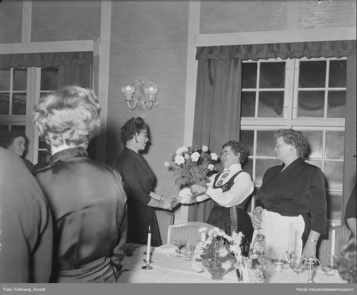 Jubilantfest 1957. Kvinne mottar blomster, kvinnelige gjester stående rundt.