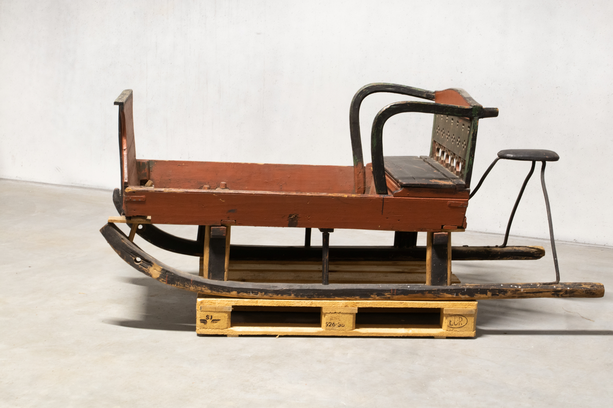 Kjelke med plan toppflate som har lave karmer på langsidene, høyt frontorett med rett topp og sveifede sidekanter. Bakerst på sluffeplanet kasseformet sete med hengslet lokk. Setet har gjennombrutt rygg og bøyleformede sidevanger. Bak på meiene skinnbetrukket kuskesete som hviler på tre bøyde jernstenger.