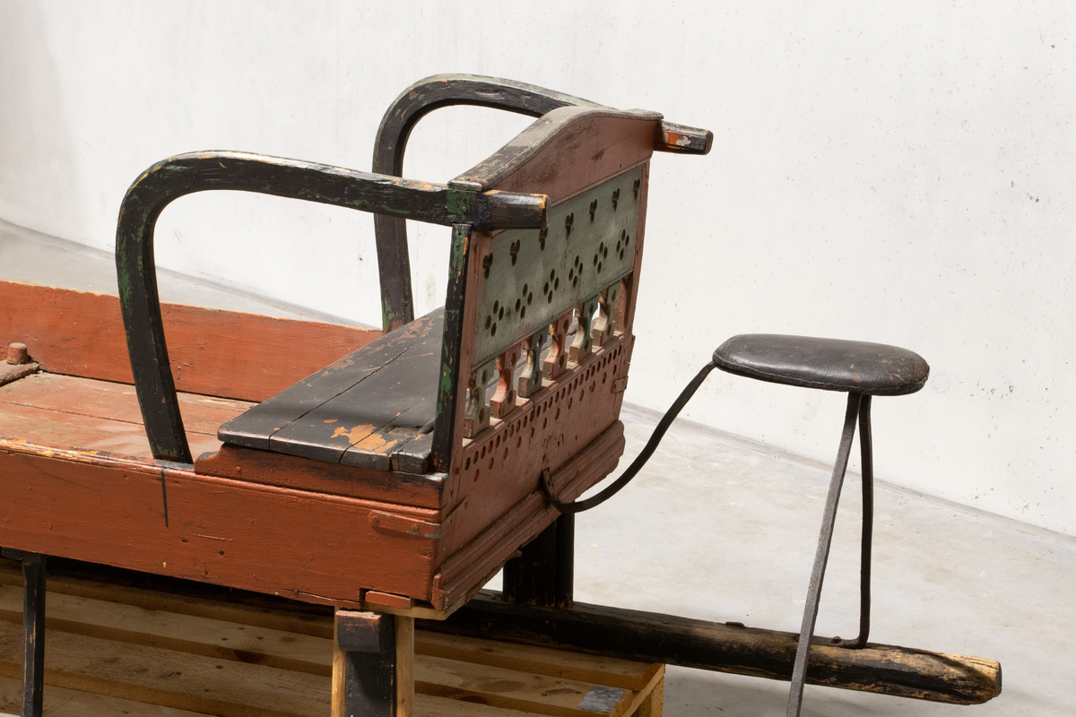 Kjelke med plan toppflate som har lave karmer på langsidene, høyt frontorett med rett topp og sveifede sidekanter. Bakerst på sluffeplanet kasseformet sete med hengslet lokk. Setet har gjennombrutt rygg og bøyleformede sidevanger. Bak på meiene skinnbetrukket kuskesete som hviler på tre bøyde jernstenger.