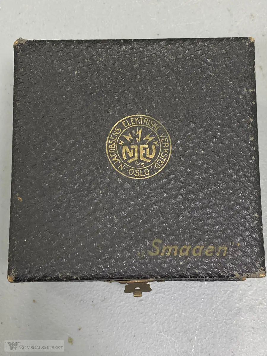 Et lite krystallapparat montert i en liten boks av trefiner eller tykk papp, kledd med sort papir. Messinglås i front.