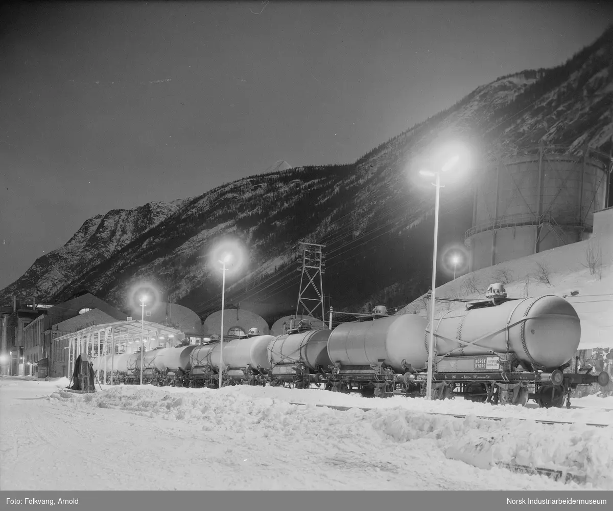 Tankvogner type Q4 stående ved NH3-tapperiet. Belysning langs tapperiets spor. N2-gasometer og Ovnshus 1 i bakgrunnen.