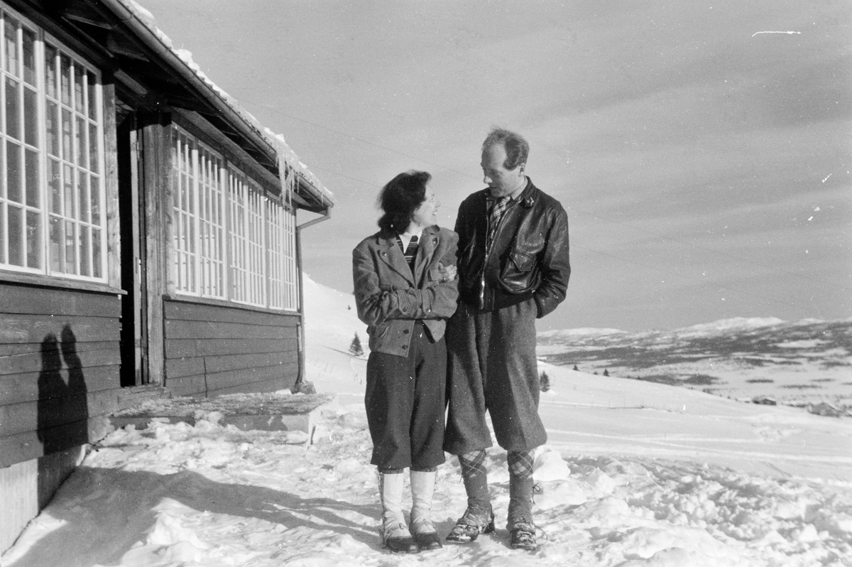 To personer står i snø utenfor hus