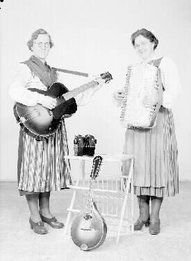 Britta Svärds orkester. Två kvinnor i folkdräkter med sina instrument, gitarr, dragspel och mandolin.