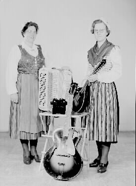 Britta Svärds orkester. Två kvinnor i folkdräkter med sina instrument, gitarr, dragspel och mandolin.