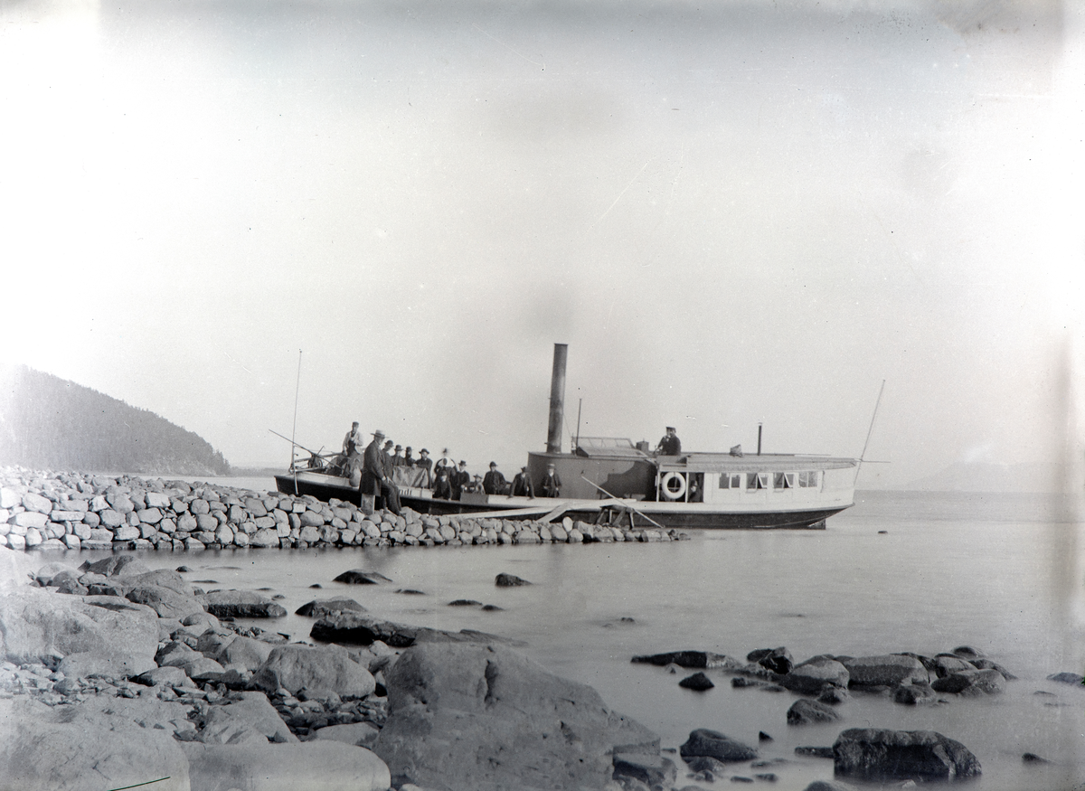 D/S Lettvindt ved Jessnes Brygge i Ringsaker. Kaptein Christian Jensen står i styrhuset. Mjøsbåt. Steinbrygge. Lettvindt var Mjøsas første propellbåt, bygd i 1867. Senere ble den ombygd og døpt Helgøy. Den endte sine dager ved Minnesund i 1960 under navnet Mira.
