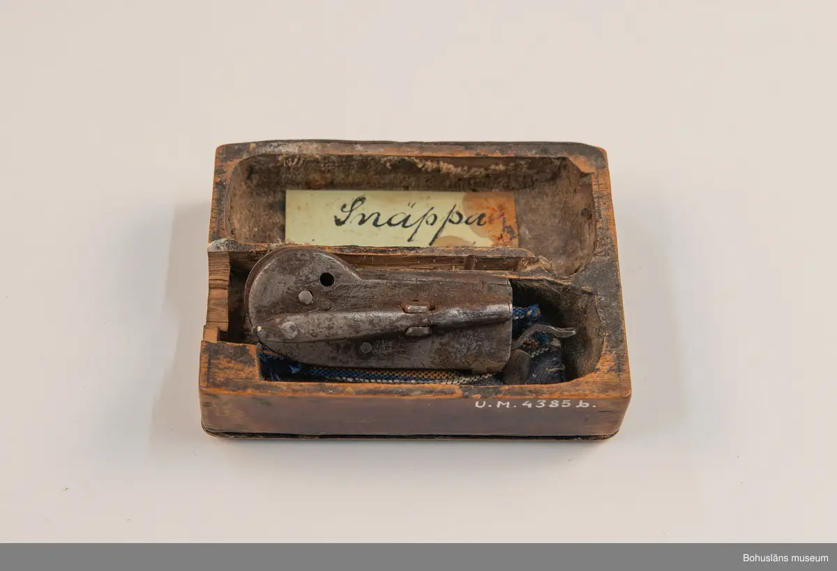 Ur handskrivna katalogen 1957-1958:
Snäppa m. fodral
Snäpparen a) L. 6,5 cm; helt av järn. Hel. Fodralet b) 8,5 x 6,5 x 2 cm; m. fack f. 2 "snäppor"; på undersid. ett lock som skyddar ett spegelglas i 2 delar. Defekt.

Lappkatalog: 94
