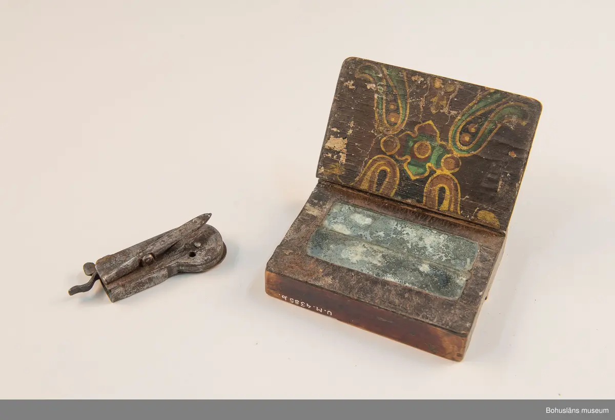 Ur handskrivna katalogen 1957-1958:
Snäppa m. fodral
Snäpparen a) L. 6,5 cm; helt av järn. Hel. Fodralet b) 8,5 x 6,5 x 2 cm; m. fack f. 2 "snäppor"; på undersid. ett lock som skyddar ett spegelglas i 2 delar. Defekt.

Lappkatalog: 94