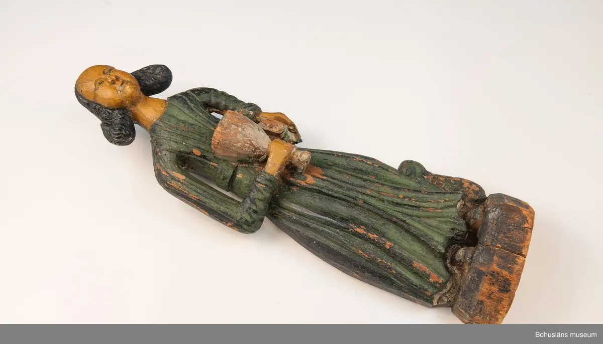 Evangelisten Johannes . Nischbild från predikstol. I höger hand kalken, i vänster hand en hopslagen bok. Vid fötterna en örn. Skägg och hår kraftigt accentuerade.
Från okänd kyrka i Bohuslän. 

Nischbild från predikstol tillsammans med skulptur UM000400.

G:14 i 1869 års tryckta katalog:
Träbeläte av S:t Johannes.

Knut Adrian Andersosns Katalog I De kyrkliga samlingarna I:124:16:
Träbild av Evangelisten Johannes
50 x 15 cm = G:14 i 1869 års rycka katalog. 
Från tiden efter 1550 i Bohuslän.,




Ur handskrivna katalogen 1957-1958:
S:t Johannes, Bohusl.
H. 48 cm; i höger hand en kalk, i vänster en hopslagen bok; dräkten målad i grönt och svart; färgen ngt. flagn. mask.

Lappkatalog: 13

Ur Nationalencyklopedin, NE.se: Evangelist
evangelist, benämning på den som enligt traditionen författat något av Nya Testamentets evangelier: Matteus, Markus, Lukas resp. Johannes
I kyrklig bildkonst framställs Matteus och Johannes ofta som äldre män, Markus och Lukas som yngre. Sedan slutet av 300-talet brukar fyra (vanligen bevingade) gestalter, evangelistsymboler, höra ihop med de fyra evangelisterna, antingen bredvid dem eller ensamma, ofta omgivande Kristus eller Lammet. Matteus representeras av en människa, Markus av ett lejon, Lukas av en tjur och Johannes av en örn. Besläktad symbolik möter i tetramorfen ("den fyrgestaltade"), ett bevingat väsen med fyra huvuden (av människa, lejon, tjur och örn), ibland också med motsvarande fötter. Symbolerna är hämtade ur Bibeln. I Hes. 1 skildras hur Hesekiel ser fyra varelser (tetramorfer) kring Guds tronvagn. I Johannes vision i Upp. 4:6-7 har de fyra varelserna kring tronen endast ett ansikte vardera: ett lejon-, tjur-, människo- eller örnansikte. Tillämpningen på evangelisterna bygger på en allegorisk tolkning av Upp. 4:6-7, belagd redan hos Irenaeus.