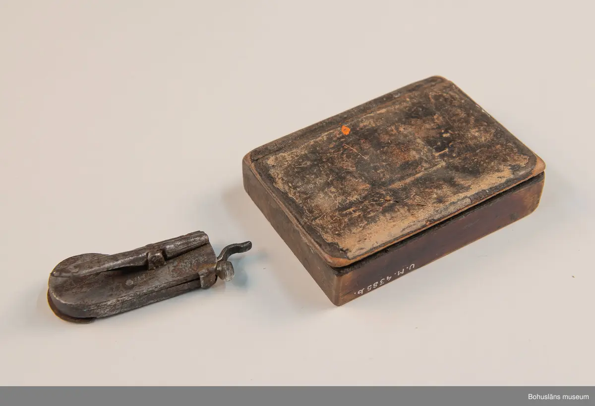 Ur handskrivna katalogen 1957-1958:
Snäppa m. fodral
Snäpparen a) L. 6,5 cm; helt av järn. Hel. Fodralet b) 8,5 x 6,5 x 2 cm; m. fack f. 2 "snäppor"; på undersid. ett lock som skyddar ett spegelglas i 2 delar. Defekt.

Lappkatalog: 94
