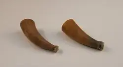 Kopphorn. Ur handskrivna katalogen 1957-1958:
Två horn för koppning
a) L. c:a 9,5 cm; av kalv, spetsen avskuren och överbunden m. tunnt skinn, sprucket; f.ö. helt. b) på undersid. ett lock som skyddar...