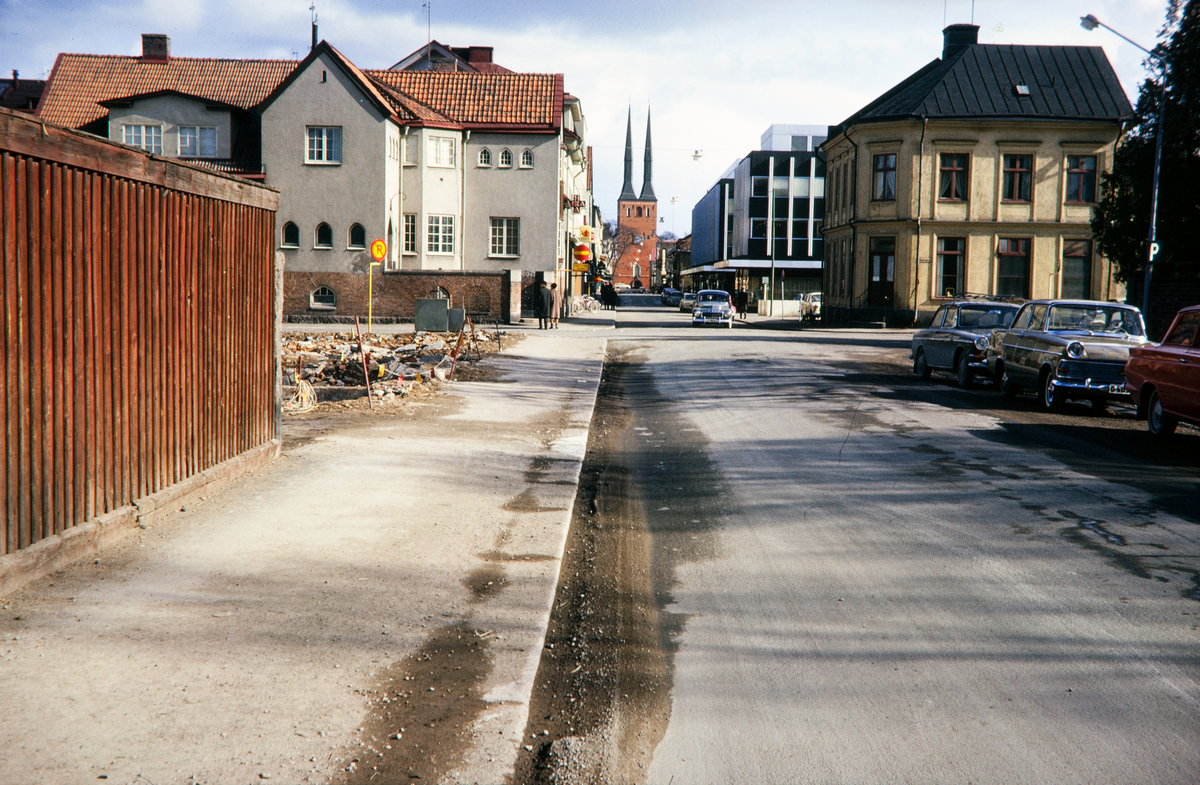 Sandgärdsgatan österut. Till vänster pågår rivningsverksamhet i kvarteret Fries, vid korsningen mot Västergatan. I bakgrunden syns några husen i kvarteret Stormen och Lugnet. 
Färgfoto ca 1965.