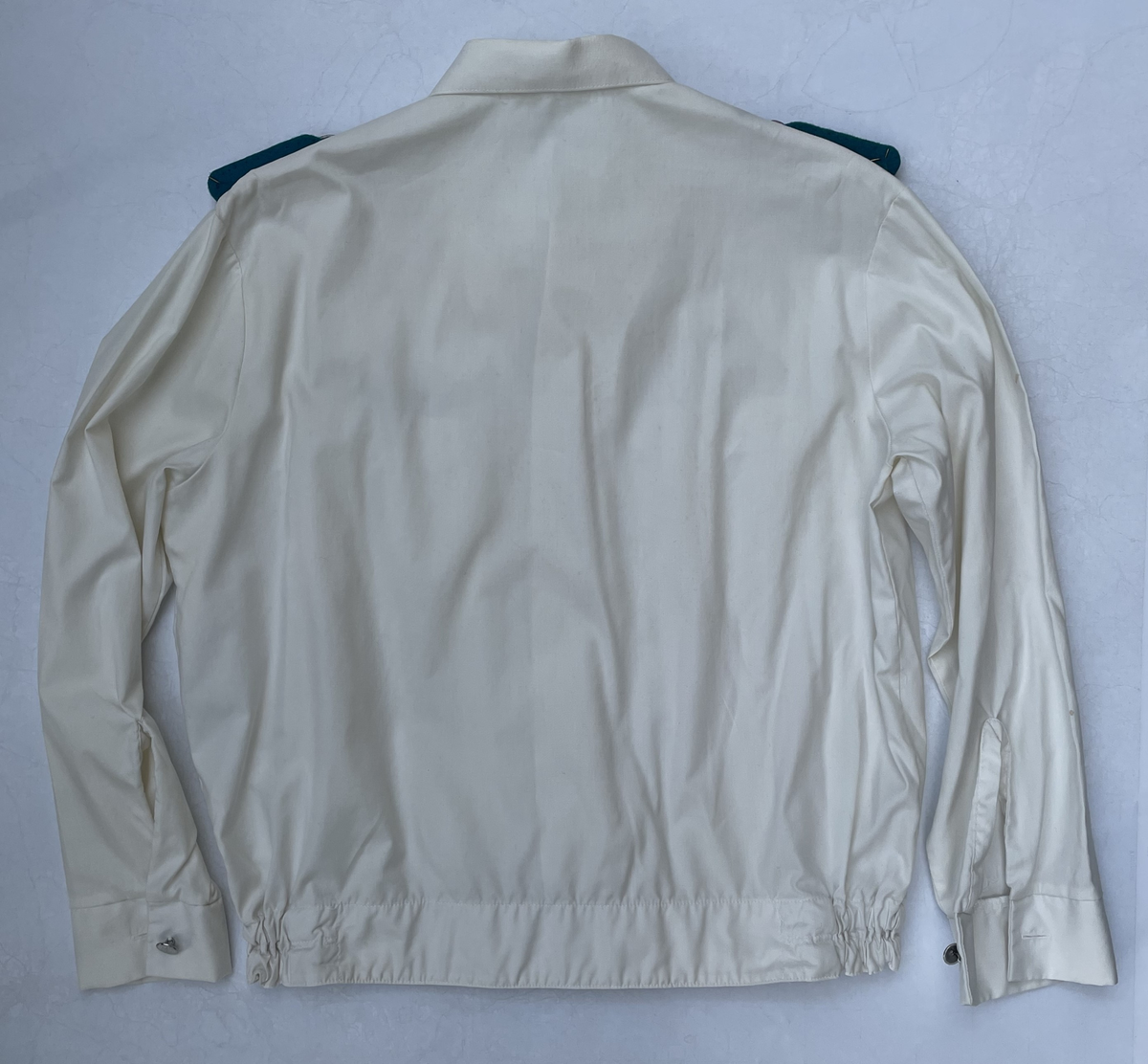 En vit skjortblus (Hemdbluse) för överstelöjtnant vid de östtyska gränstrupperna (Grenztruppen der DDR). Storlek 42N. Skjortblusen ingick i stabsuniform sommar (Stabsdienstuniform Nr. 2 So) och bars utan skjorta under.
Över höger bröstficka sitter en minnesmedalj för östtyska armens (Nationalen Volksarmee – NVA) 30-års jubileum. På nålfästet texten ”1956-1986”, på medaljens framsida ”30 JAHRE NATIONALE VOLKSARMEE” och på frånsidan ”Fest verwurzelt im Volk, gefürt von der Partei, erfüllen wir den Klassenauftrag. Forwärts zom XI. Parteitag der SEDI”.
Över vänster bröstficka sitter släpspännen. 
I övre raden band för (från höger till vänster från betraktarens håll); Vapenbrödramedaljen (Medaille der Waffenbrüderschaft) i brons och östtyska armens förtjänstmedalj (Verdienstmedaille der Nationalen Volksarmee) i brons, silver och guld.
I undre raden band för (från höger till vänster från betraktarens håll); medaljen för trogen tjänst i östtyska gränstrupperna (Medaille für treue Dienste in den Grenztruppen der DDR) 5 års tjänst, 10 års tjänst, 15 års tjänst och 20 års tjänst.
