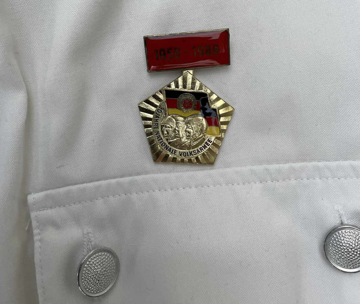 En vit skjortblus (Hemdbluse) för överstelöjtnant vid de östtyska gränstrupperna (Grenztruppen der DDR). Storlek 42N. Skjortblusen ingick i stabsuniform sommar (Stabsdienstuniform Nr. 2 So) och bars utan skjorta under.
Över höger bröstficka sitter en minnesmedalj för östtyska armens (Nationalen Volksarmee – NVA) 30-års jubileum. På nålfästet texten ”1956-1986”, på medaljens framsida ”30 JAHRE NATIONALE VOLKSARMEE” och på frånsidan ”Fest verwurzelt im Volk, gefürt von der Partei, erfüllen wir den Klassenauftrag. Forwärts zom XI. Parteitag der SEDI”.
Över vänster bröstficka sitter släpspännen. 
I övre raden band för (från höger till vänster från betraktarens håll); Vapenbrödramedaljen (Medaille der Waffenbrüderschaft) i brons och östtyska armens förtjänstmedalj (Verdienstmedaille der Nationalen Volksarmee) i brons, silver och guld.
I undre raden band för (från höger till vänster från betraktarens håll); medaljen för trogen tjänst i östtyska gränstrupperna (Medaille für treue Dienste in den Grenztruppen der DDR) 5 års tjänst, 10 års tjänst, 15 års tjänst och 20 års tjänst.