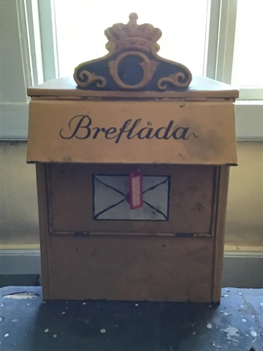 Brevlåda av koppar. Gulmålad. På locket skrivet med svart färg: "Breflåda". Under locket: ett brev målat i vitt och svart med rött sigill. Högst uppe på framsidan postens "vapen" i gult, blått och rött. 