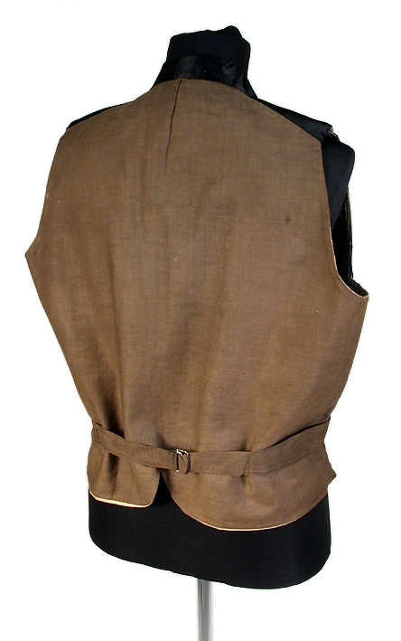 Väst av svart siden med stora slag, dubbelknäppt, 4 flata, små sidenöverklädda knappar i var rad. Två raka fickor. Gult linnefoder. I kanten och på ryggens baksida, brunt linnelärft. (På vänstra sidan nedtill ligger insytt 1 hålsmatt, hårt föremål.