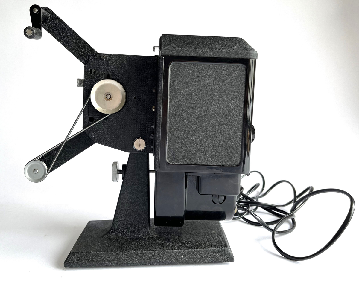 Filmkamera av Agfa, Movector 8. Elektrisk filmredigerings-apparat i opprinnelig eske. Produsert mellom 1938 - 1944. For avspillingen av dubbel8-filmer.
Esken fungerer som en koffert, med håndtak, jernbeslag og 4 store jernnagler på basen. Laget av papp, dekket med brun syntetisk skinn. Inni er noen treklosser for å holde kameraet, sammen med en svart bomullsstropp med spenne.