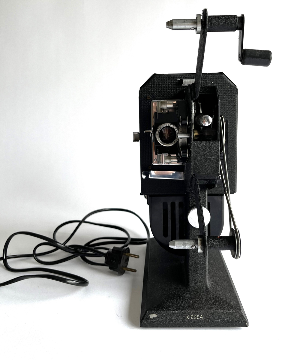 Filmkamera av Agfa, Movector 8. Elektrisk filmredigerings-apparat i opprinnelig eske. Produsert mellom 1938 - 1944. For avspillingen av dubbel8-filmer.
Esken fungerer som en koffert, med håndtak, jernbeslag og 4 store jernnagler på basen. Laget av papp, dekket med brun syntetisk skinn. Inni er noen treklosser for å holde kameraet, sammen med en svart bomullsstropp med spenne.