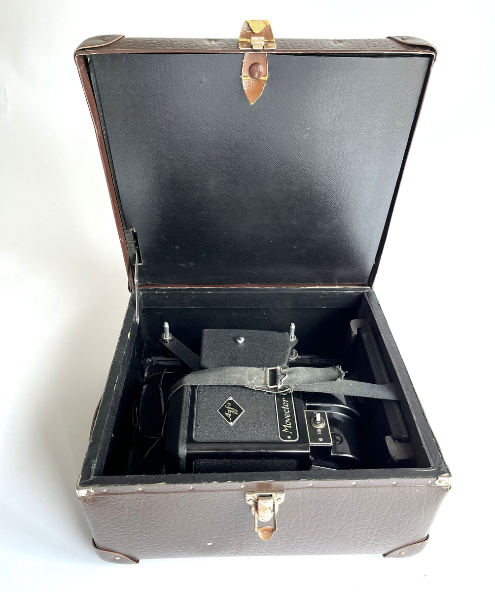 Filmkamera av Agfa, Movector 8. Elektrisk filmredigerings-apparat i opprinnelig eske. Produsert mellom 1938 - 1944. For avspillingen av dubbel8-filmer.
Esken fungerer som en koffert, med håndtak, jernbeslag og 4 store jernnagler på basen. Laget av papp, dekket med brun syntetisk skinn. Inni er noen treklosser for å holde kameraet, sammen med en svart bomullsstropp med spenne.