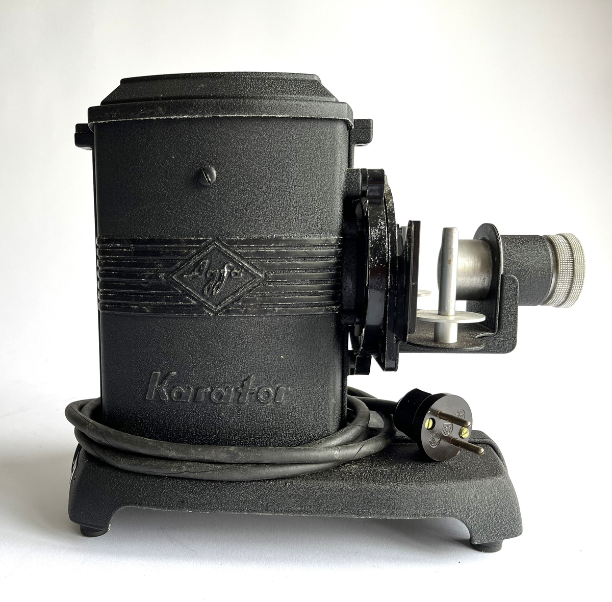 Fremviser. Elektrisk lysbildefremviser av Agfa i brun pappeske med håndtak og enkel lås. Modell Karator II. Lysbildefremviserobjektiv merket Agfa Agomar 75/2.8. Karator II- fremviser kan kaste lysbilder i formatet "35 mm (5 x 5 cm ytre mål)" og bildebånd (filmbånd) i formatet "35 mm film" på veggen.
Ufullstendig: Denne mangler fester for filmstripsspoler (kun stål stang). Esken/etuiet fremstår som opprinnelig, men mangler Agfa-merket trykket på lokket. Gjenstanden har også en "Zum apparat" av Agfa som tilbehør.