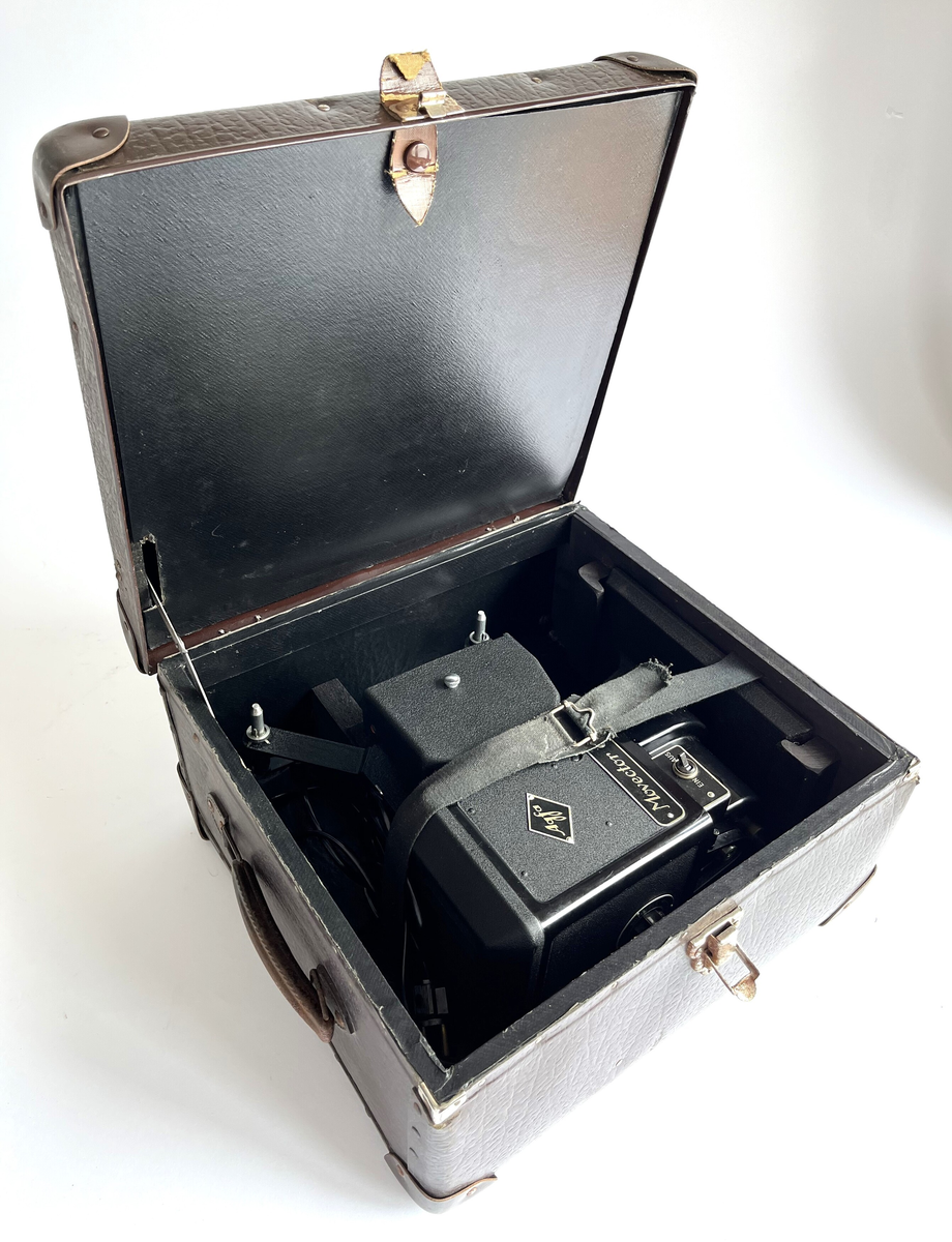 Filmkamera av Agfa, Movector 8. Elektrisk filmredigerings-apparat i opprinnelig eske. Produsert mellom 1938 - 1944. For avspillingen av dubbel8-filmer.
Esken fungerer som en koffert, med håndtak, jernbeslag og 4 store jernnagler på basen. Laget av papp, dekket med brun syntetisk skinn. Inni er noen treklosser for å holde kameraet, sammen med en svart bomullsstropp med spenne.