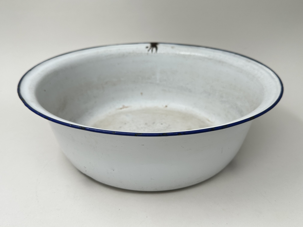 Skål, av emaljerad metall. Vit emalj med rullad blå kant. Stämpel i botten. Emaljen kantstött.