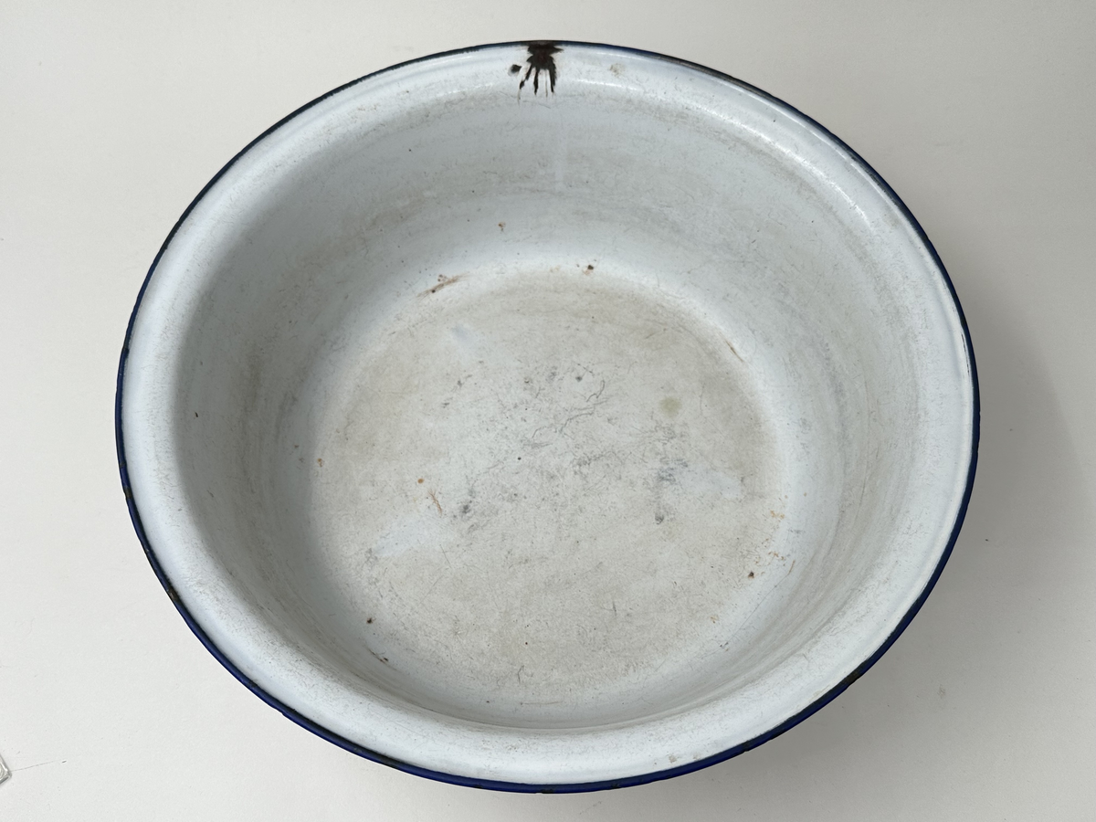 Skål, av emaljerad metall. Vit emalj med rullad blå kant. Stämpel i botten. Emaljen kantstött.