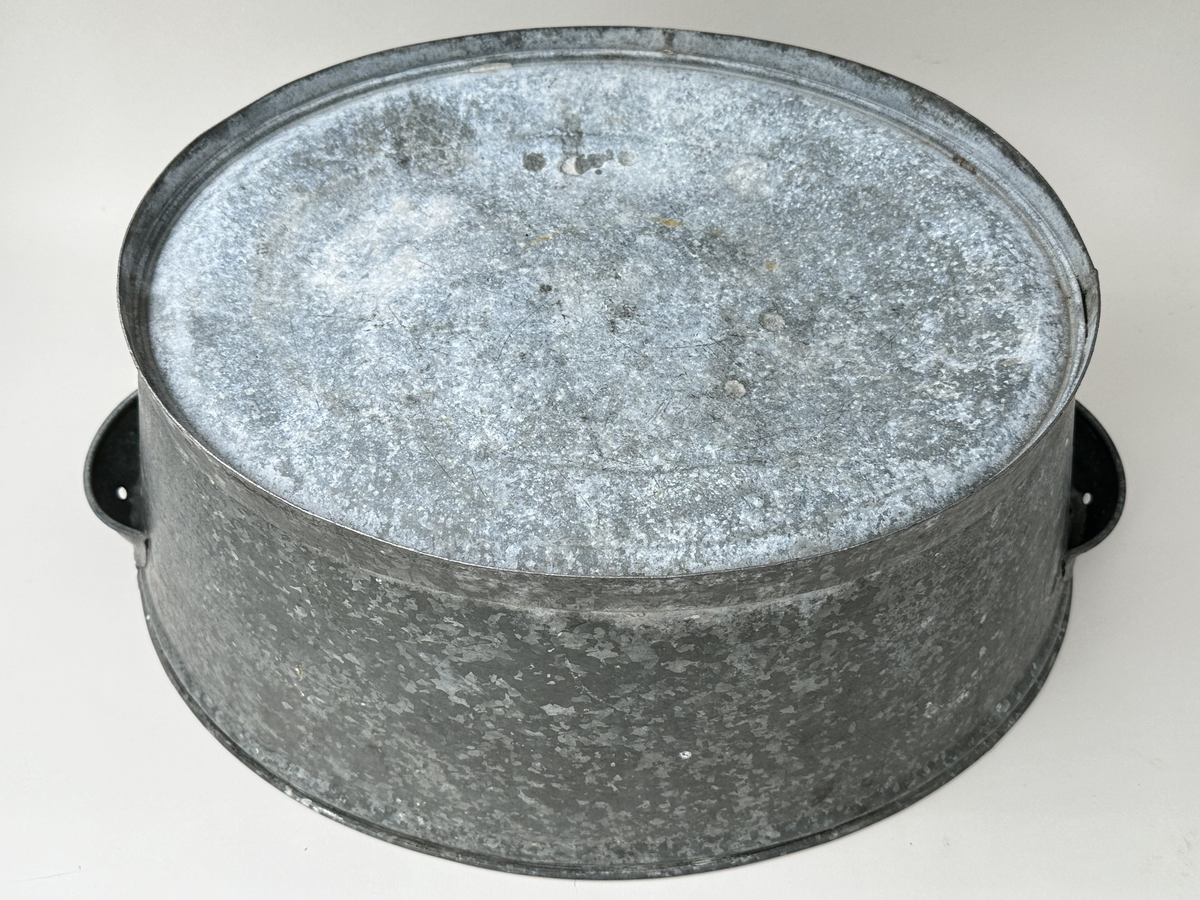 Balja, diskbalja av galvaniserad plåt. Oval form, med ett skålhandtag på var kortsida. 