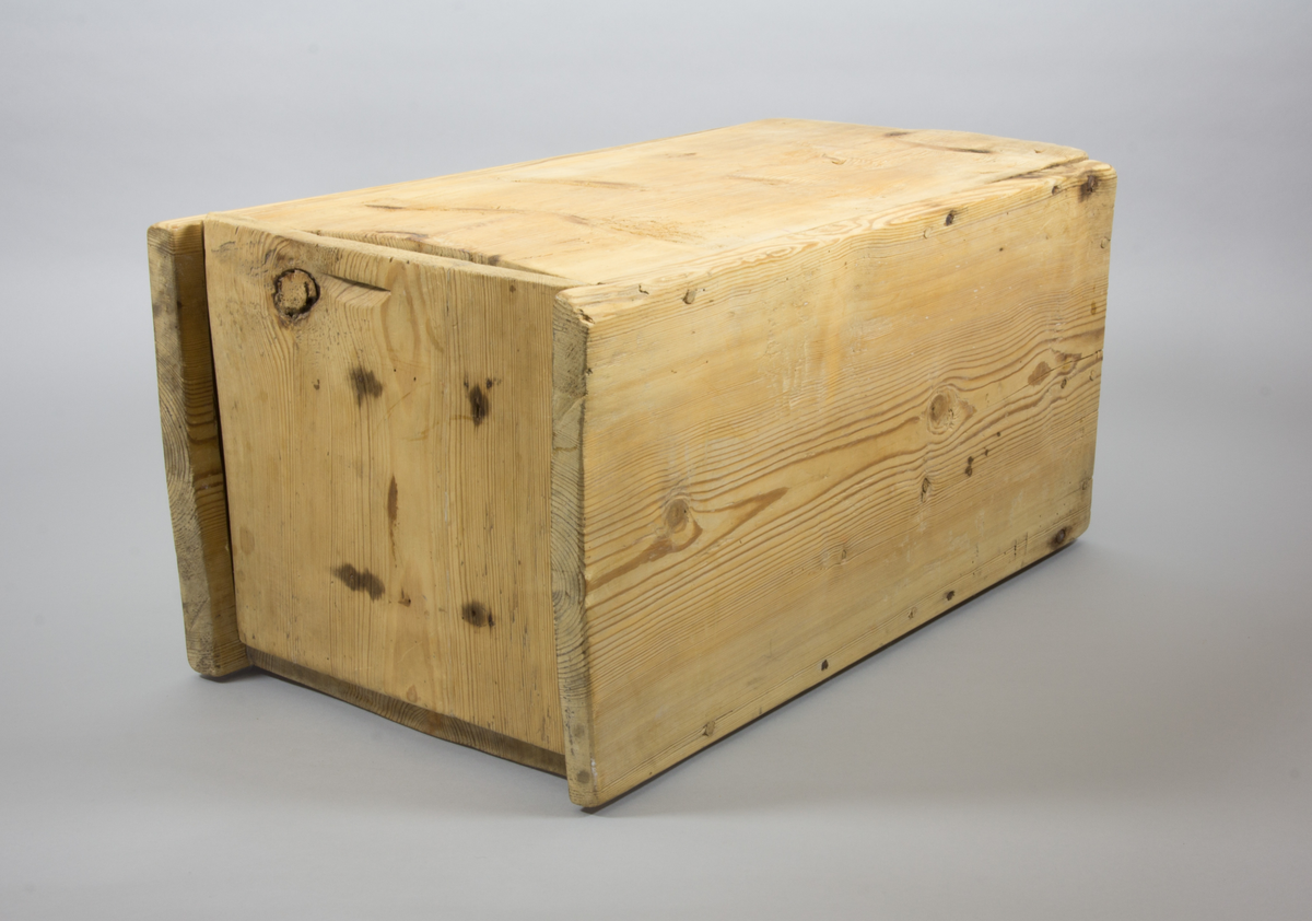 En låda tillverkad i trä. Rektangulär med raka sidor. Längst upp finns ett lock som går att fästa i en skåra i sidorna.