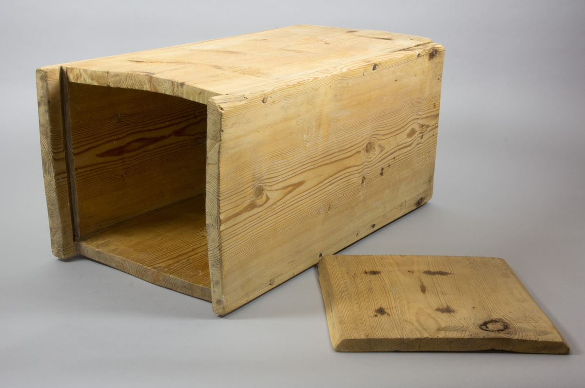 En låda tillverkad i trä. Rektangulär med raka sidor. Längst upp finns ett lock som går att fästa i en skåra i sidorna.