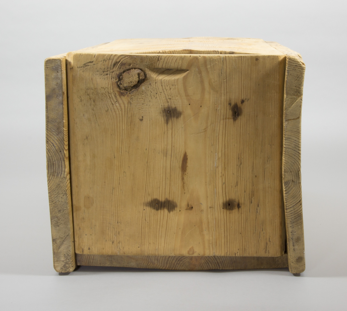 En låda tillverkad i trä. Rektangulär med raka sidor. Längst upp finns ett lock som går att fästa i en skåra i sidorna.