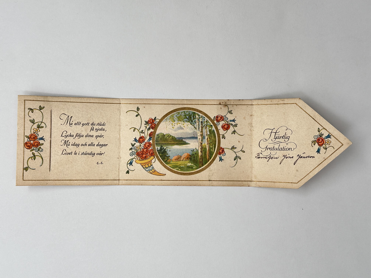 Gratulationskort i papper. Hopvikbart så det ser ut som kuvert med snöre om, sigill och adressblad. Inuti tecknade blommor och blad samt rund bild föreställande sommarlandskap med sjö och björkar. Tryckt dikt. 