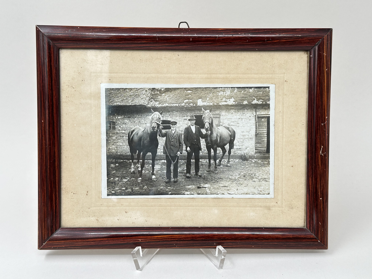 Fotografi i ram. Svartvitt fotografi föreställande Per Åkesson tillsammans med en av hans söner hållandes i varsin häst, Fux och Stjärna, framför gården Hög 18:1. Runt fotografiet passepartout av beige kartong. Ramen ådringsmålad i brunt, med glasfront och baksida av kartong som är fäst med stift och förseglat med klisterremsa. Hängare av en tunn märla av ståltråd.
