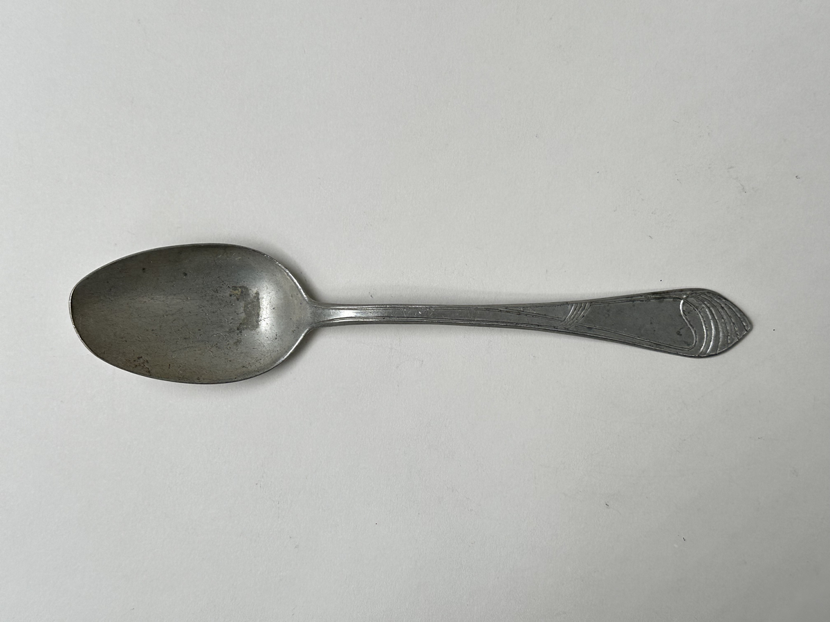 Sked i aluminiumlegering. Dekor av slingor i jugendstil på skaftet. Oregelbunden form på bladet. 