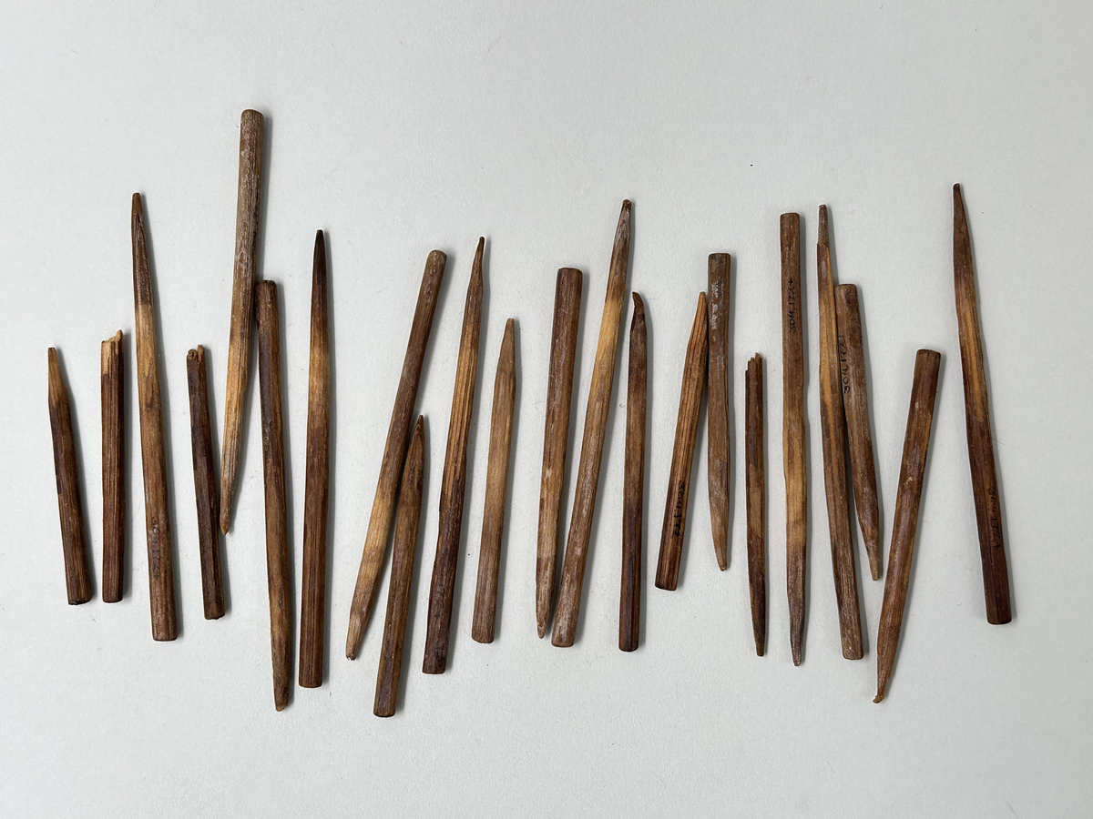 Korvstickor, 22 stycken, handskurna av trä som mörknat av användning. Varierande mått, vissa avbrutna. Förvaras i cigarrask av trä, med lock som en gång varit fäst till asken genom klot men nu lossnat. Asken dekorerad med pålimmade tryckta pappersremsor i svart och rött. "CLARO" inbränt på askens ena sida. På lockets utsida prislapp i grönt samt ett nedsänkt företagsemblem, insidan locket klätt med papper varpå företagsemblemet tryckts i grön färg.